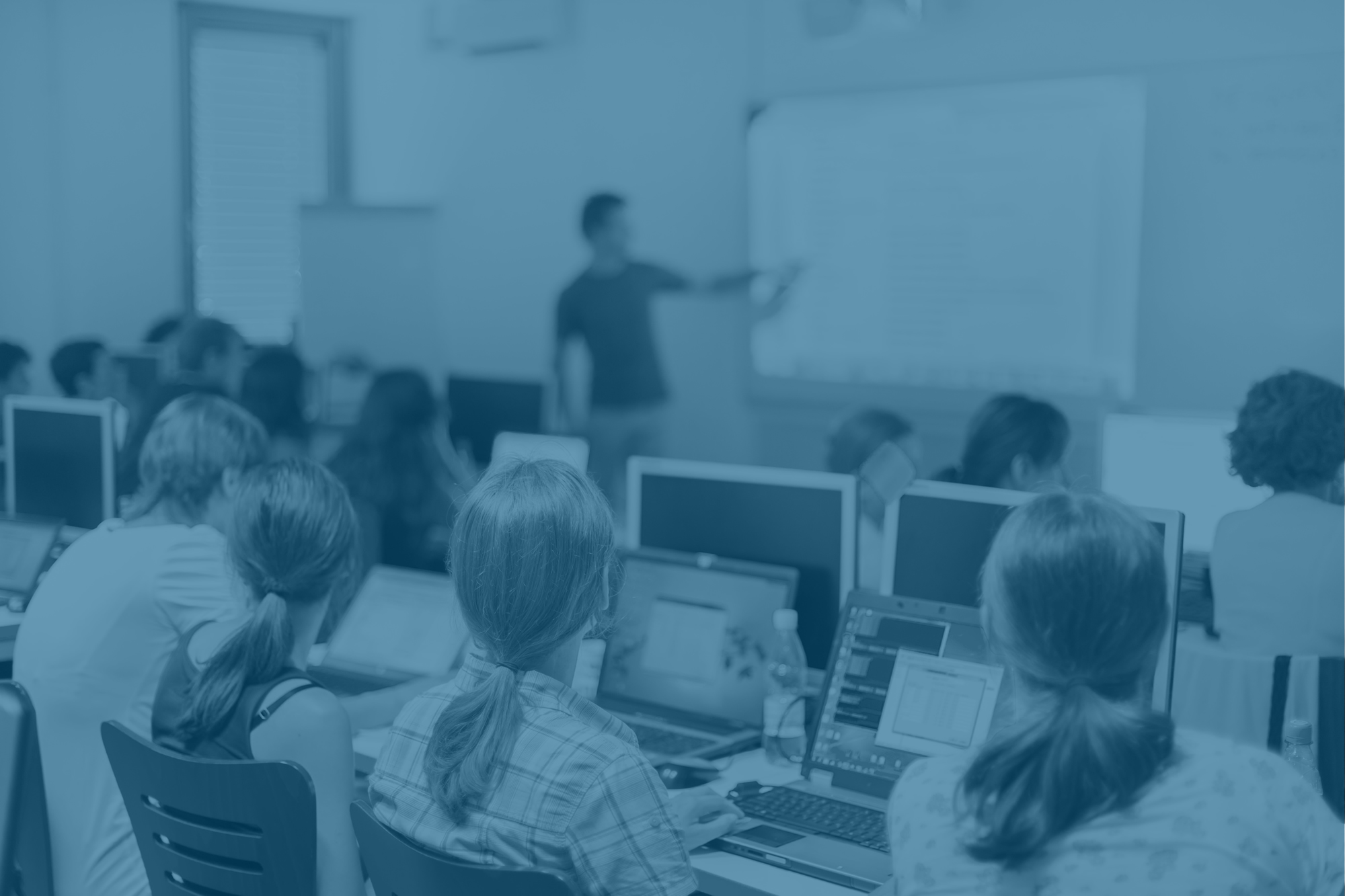 Image of man pointing to a whiteboard in a training room with a number of students watching