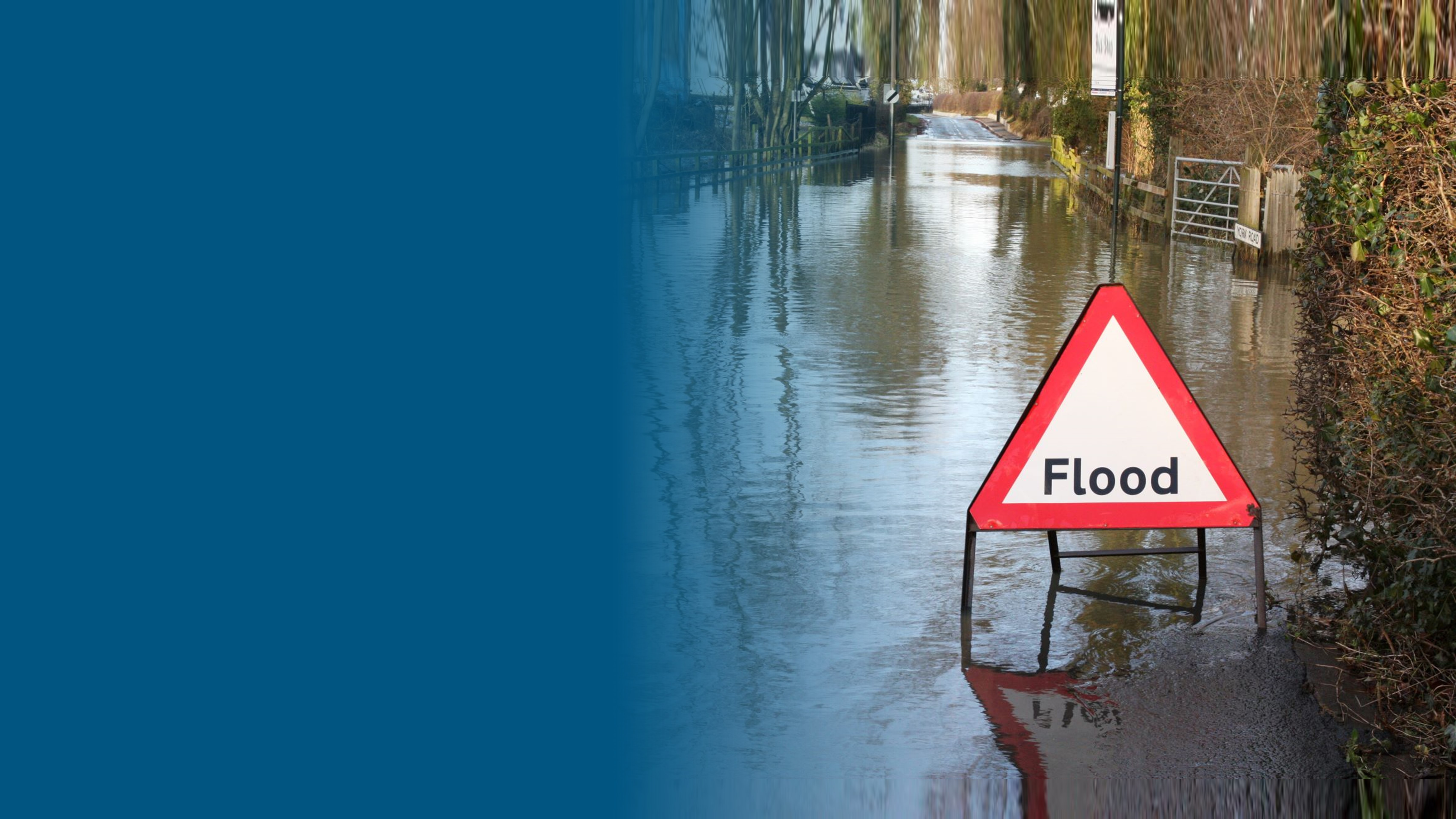 An image of a flood sign in the street with flooding around it